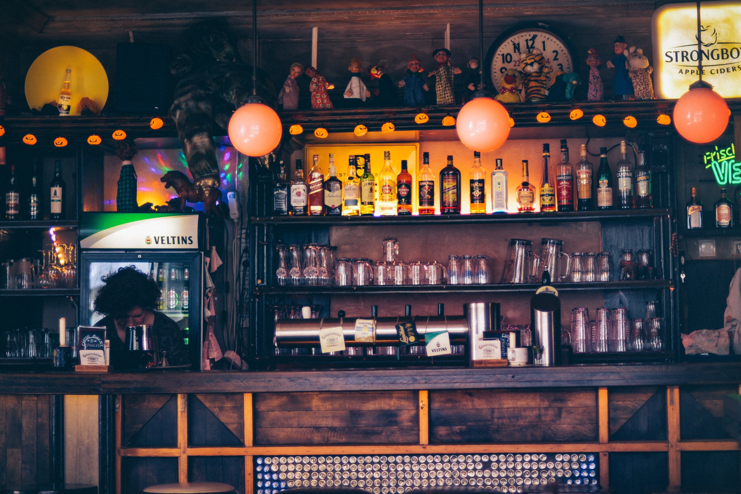 person sitting near wooden desk and shelf of bottles